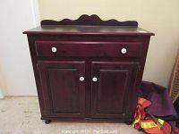 Front view of dark wood cabinet showing drawer and double doors with white knobs.