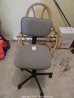 Gray fabric adjustable office chair with black swivel base and backrest, placed in front of rattan chair.