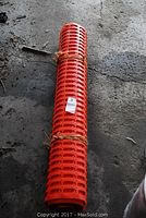 Full view of the rolled orange plastic snow fence secured with twine, lying on a concrete floor.