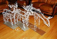 Three white wire frame reindeer Christmas decorations placed on a wooden floor with attached string lights on plywood bases, showing overall condition and dimensions.