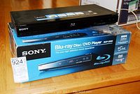 Sony BDP-S360 Blu-ray Disc/DVD player sitting on its original blue product box on a wooden surface, showing front panel and top.