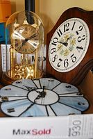 Three clocks shown: anniversary clock with gold elements under glass dome, round stained glass clock, wooden clock with floral design.