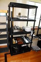 Full view of the black heavy plastic shelving unit showing four shelves with various household items placed on it to illustrate size and capacity.