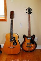 Both guitars side by side against wall and floor