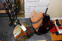 Fireplace tools on a stand next to a metal ash can, log blanket, log basket, and bellows.