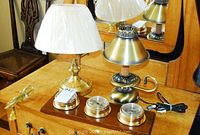 Photo showing two brass bedside lamps and a metal barometer set on a wooden dresser with mirror.