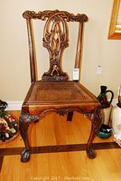 Front view of solid wood chair showing ornate carved back, legs and caned seat.