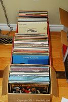 Boxes full of vintage vinyl albums stacked on wooden floor, showing variety of album spines and covers including 'The Sound of Music' soundtrack and André Gagnon.