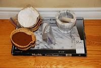 Full set showing marble mortar and pestle on marble pastry board with scallop shells in wicker baskets.