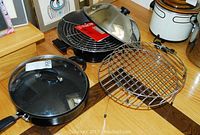 Photo showing Bialetti covered frying pan, Charlescraft electric wok with glass lid, and multiple stainless steel cooking racks on wooden table.