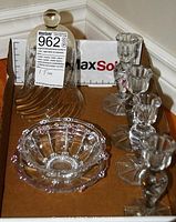 Four clear crystal candle holders with octagonal bases, two hobnail glass bowls (one with pink rim), and one clear glass bell cover with round knob top shown on a brown surface with MaxSold label.