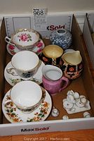 All items collectively displayed in cardboard box including teacups with saucers, cream and sugar set, ginger jar, and miniature tea set