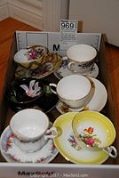 Six tea cups and saucers, various floral designs, displayed in cardboard box.