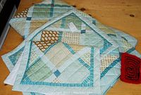 Photo showing folded patchwork comforter and a red pot holder on a wooden surface.
