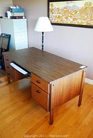 Office desk with drawers and floor lamp beside it, showing woodgrain finish and keyboard tray pulled out