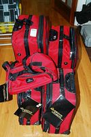 Photo showing top view of four red McBrine luggage pieces with tags, including three wheeled suitcases and one carry-on bag.