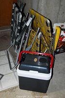 Folded vintage lawn chairs with webbing and electric car cooler in front on tile floor.