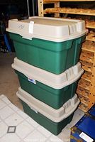 Stack of three green storage totes with beige lids in a shelving area, showing overall condition and stacking.