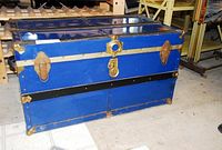 Full view of vintage blue metal steamer trunk with three metal latches and corner protectors, showing overall external condition and size.