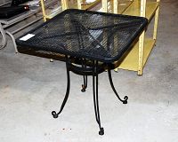Square black metal mesh garden table full view showing curved legs with curled ends and overall build.
