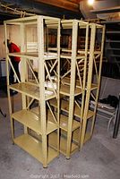 Three beige metal utility shelving units with five shelves each, showing some surface rust and age wear.