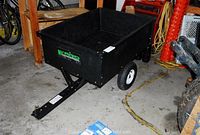 Wide angle of the black Yard Commander trailer on two wheels with a large black bed and a tongue for towing.