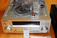 Front view of the Pioneer AV receiver silver model with knobs, display, remote, cables in plastic bags on top.