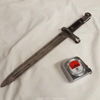 Full view of vintage metal bayonet laid next to 12 ft tape measure showing length.