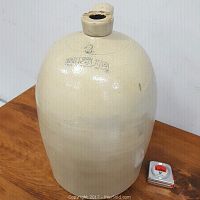 Large beige 16 inch stoneware jug with handle and small chip near the spout, placed next to 12 inch tape measure for scale.