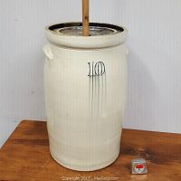 Front view of the stoneware butter churn with wooden paddle and lid, showing the '10' marking.