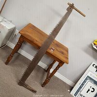 Full view of 62-inch antique two-man crosscut saw leaning against a wooden table, showing long blade and handles.