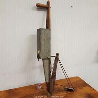 Front side view of antique corn planter showing wooden handle and metal seed hopper.