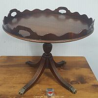 Front and side view of the mahogany lazy Susan server table showing the scalloped edged top with integral handles, fluted pedestal, and metal claw feet on curved legs. A tape measure in front for scale.
