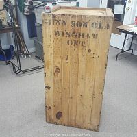 Front view of the large wooden crate showing vertical planks and stenciled lettering 'GUNN SON OLA WINDHAM ONT'.