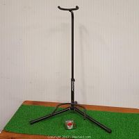 Full view of the black metal guitar or bass stand with tripod base on a green carpet