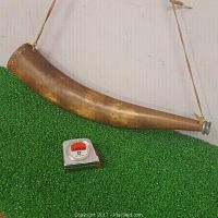 Side view of the antique moose call resting on green turf with a tape measure for scale.