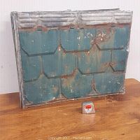 Stack of eight vintage metal roofing sheets with visible rust and green paint resting on a wooden surface, showing weathered and aged condition.