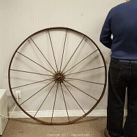 Front view of large steel wheel against a wall with a person nearby for scale, showing the full circular shape and spokes.