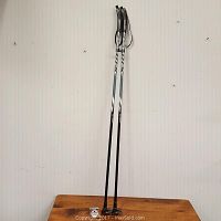 Two black and gray Swix aluminum walking sticks, standing upright on a wooden surface against a white wall.