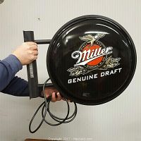 Photo of the Miller Genuine Draft light-up bar sign with the mounting bracket and electrical cord held by a person for scale.