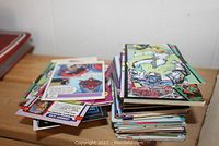 Pile of assorted colorful collectible superhero trading cards with various comic character artwork spread loosely on a wooden surface.