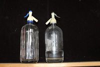Two vintage glass spritzer bottles side by side on a dark surface, showing overall appearance and structure.