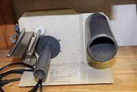 Front and side view of the beige metal Grip-A-Tab LH-31 electric tape dispenser showing tape holder, rollers, and cutting mechanism.