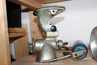 Metal manual meat grinder with clamp and black knobs shown on wood shelf.