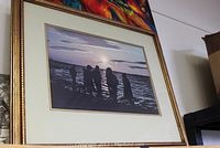 Framed photographic print showing silhouetted figures on a beach at sunset, framed in gold-finished wood frame with double mat.