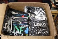 Box containing multiple new bags and purses by Jay Joshua with city-themed designs including Niagara Falls and London.