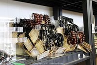 View of multiple semi-precious stone bracelets arranged on clear Lucite stands, showing tags and polished stones in brown and black shades.