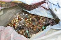 Bag filled with a mix of colorful beaded bracelets and necklaces, some appear to be made of wood and metal beads.