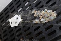 Close-up of a new dangling Noblesse Collection necklace with silver chain and iridescent small disc embellishments on plastic packaging with attached earrings on a white card.