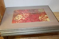 Stack of four framed textile art pieces showing fabric with red, gold, and brown floral and circular patterns in silver-tone frames